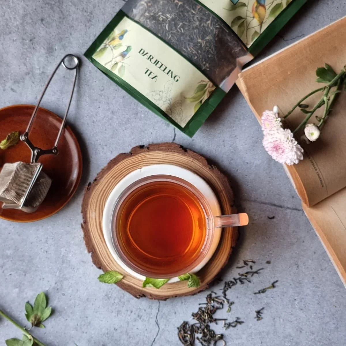 Cup of premium Darjeeling tea with loose leaves, tea infuser, and floral decor on a table